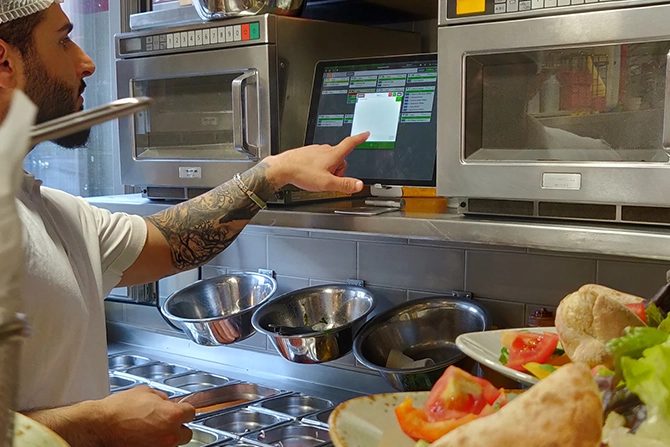 Koch tippt am Gastronovi Küchenmonitor in einer Restaurantküche eine Bestellung an